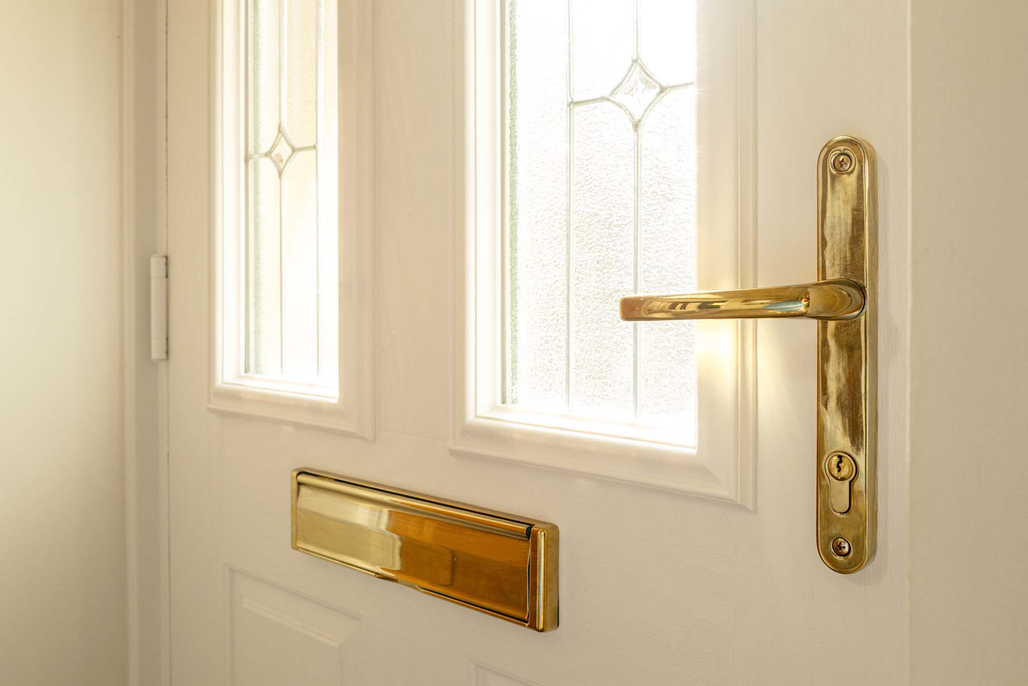 Shallow focus of a brass effect, new generation door lock and handle seen on a newly fitted, double glazed front door. Showing its double glazed,leaded windows.